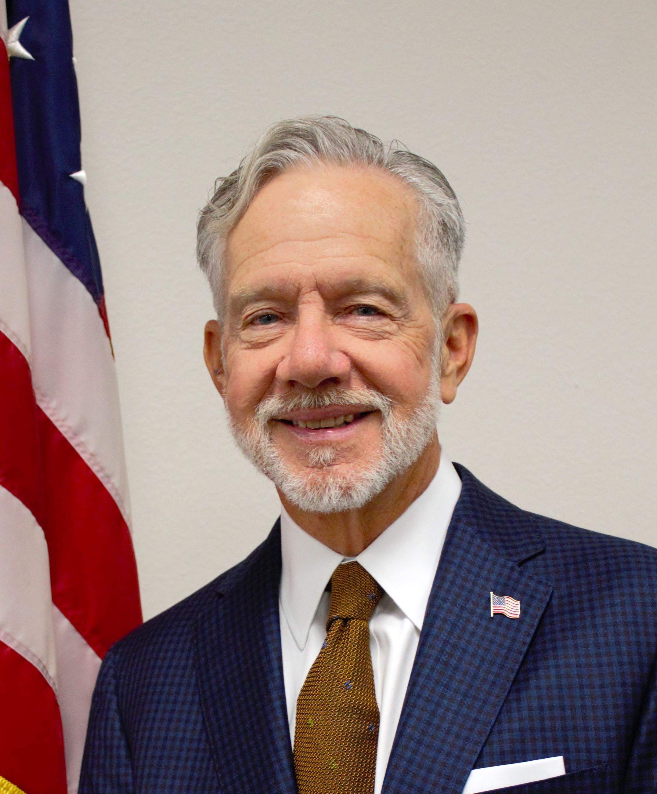 Commissioner Kelly smiles with the American flag behind him. 