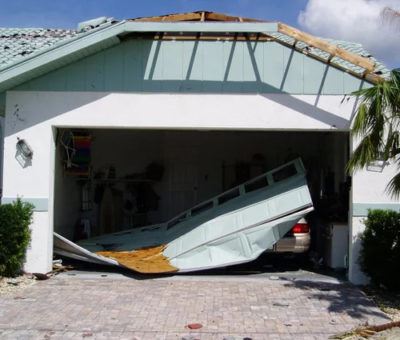 A garage door is seen crushed and detached from a home, as a result of storm damage.