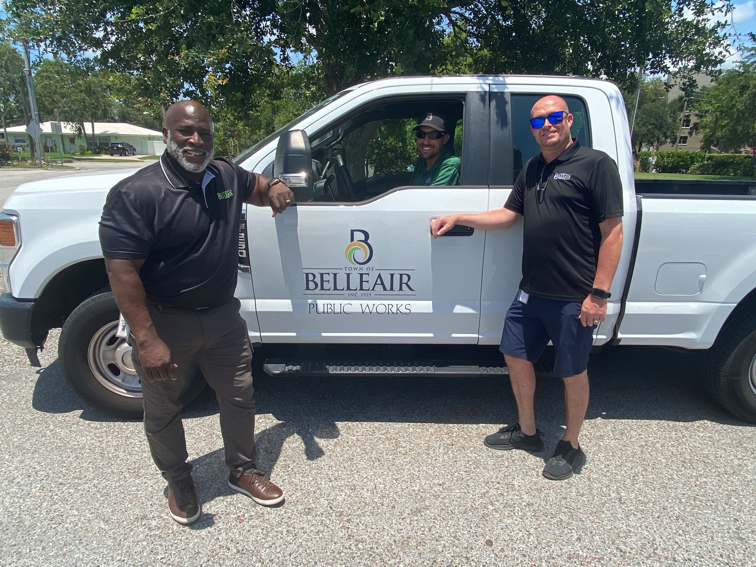 Public Works Management staff smile and pose for a photo around a work truck. 